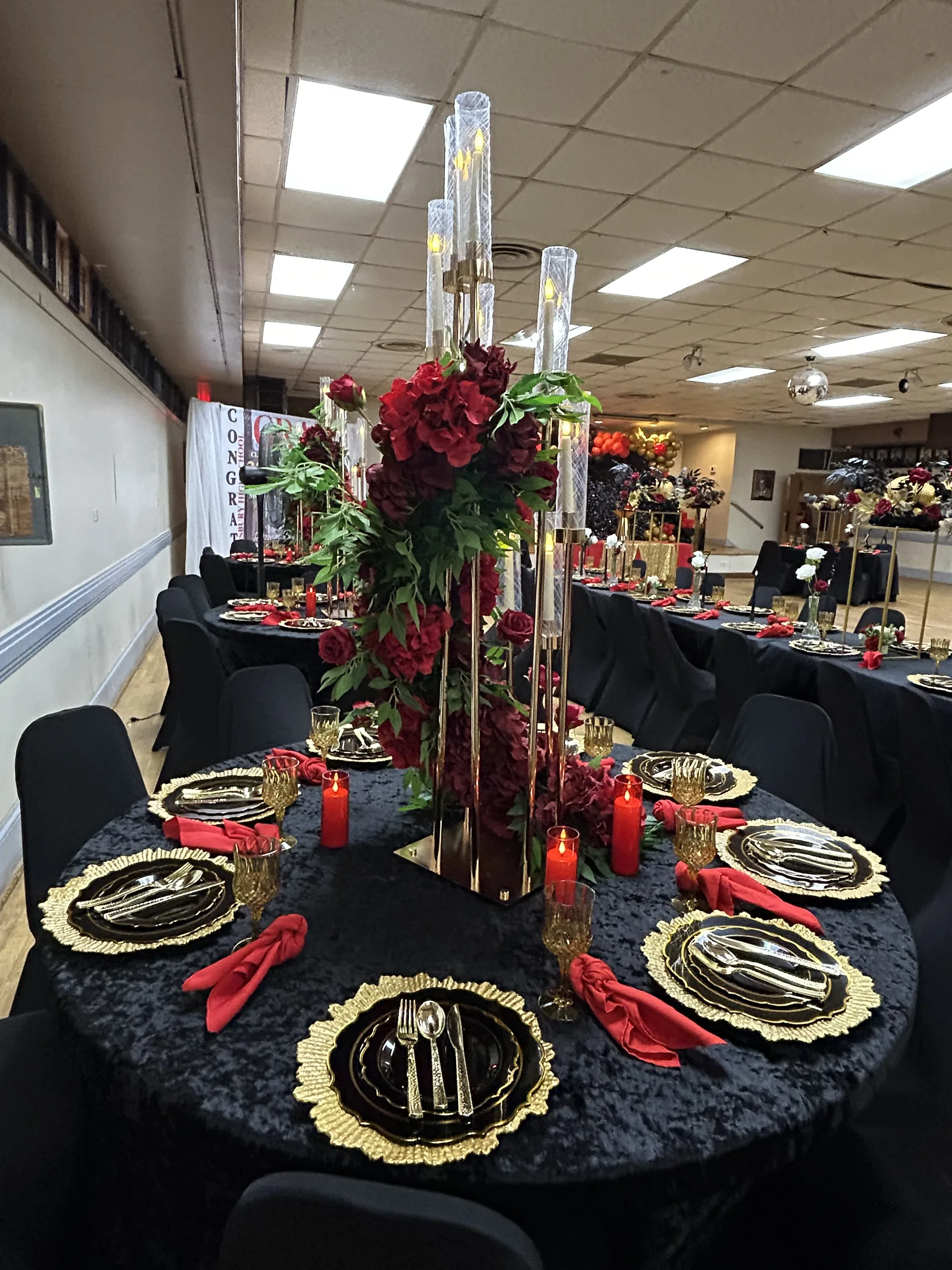 Full black velvet graduation table setup with red florals and gold chargers