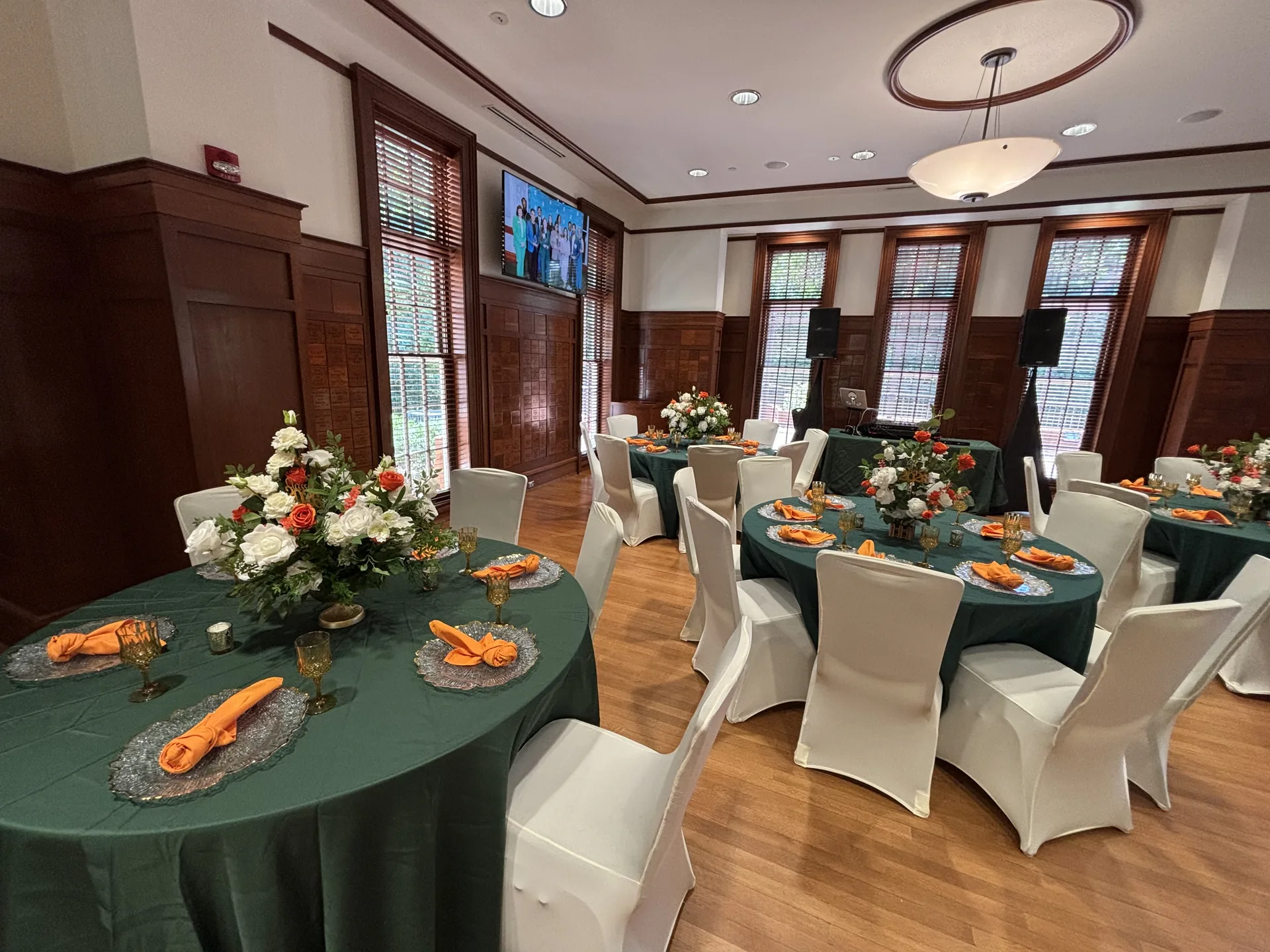 Wide event room setup with emerald table linens, florals, and gold accents
