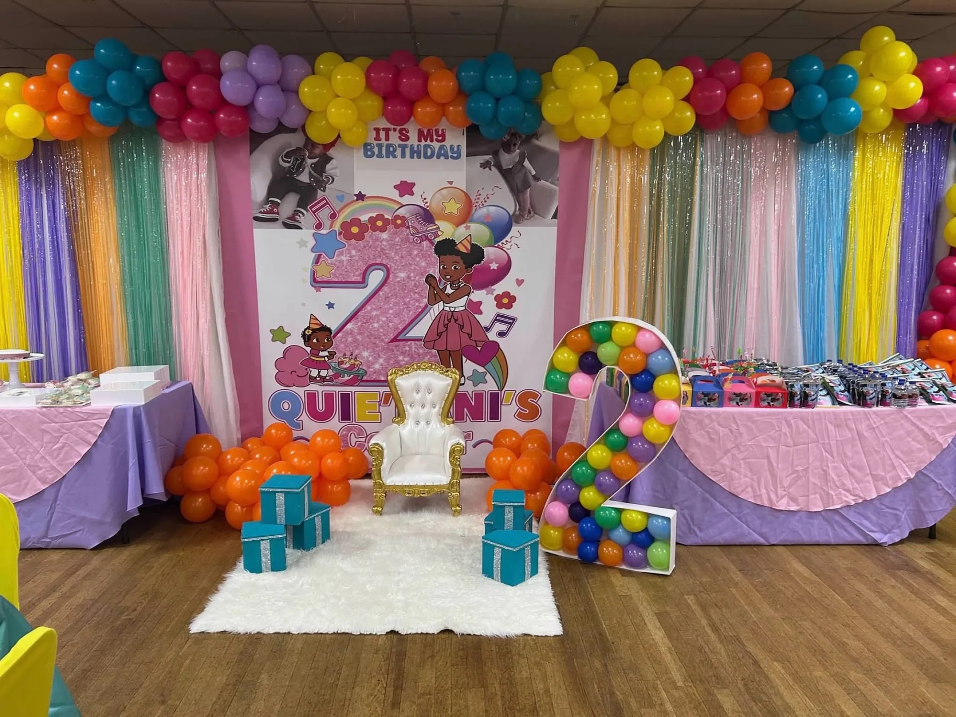 Colorful second birthday backdrop with balloon garland, throne chair, and balloon number