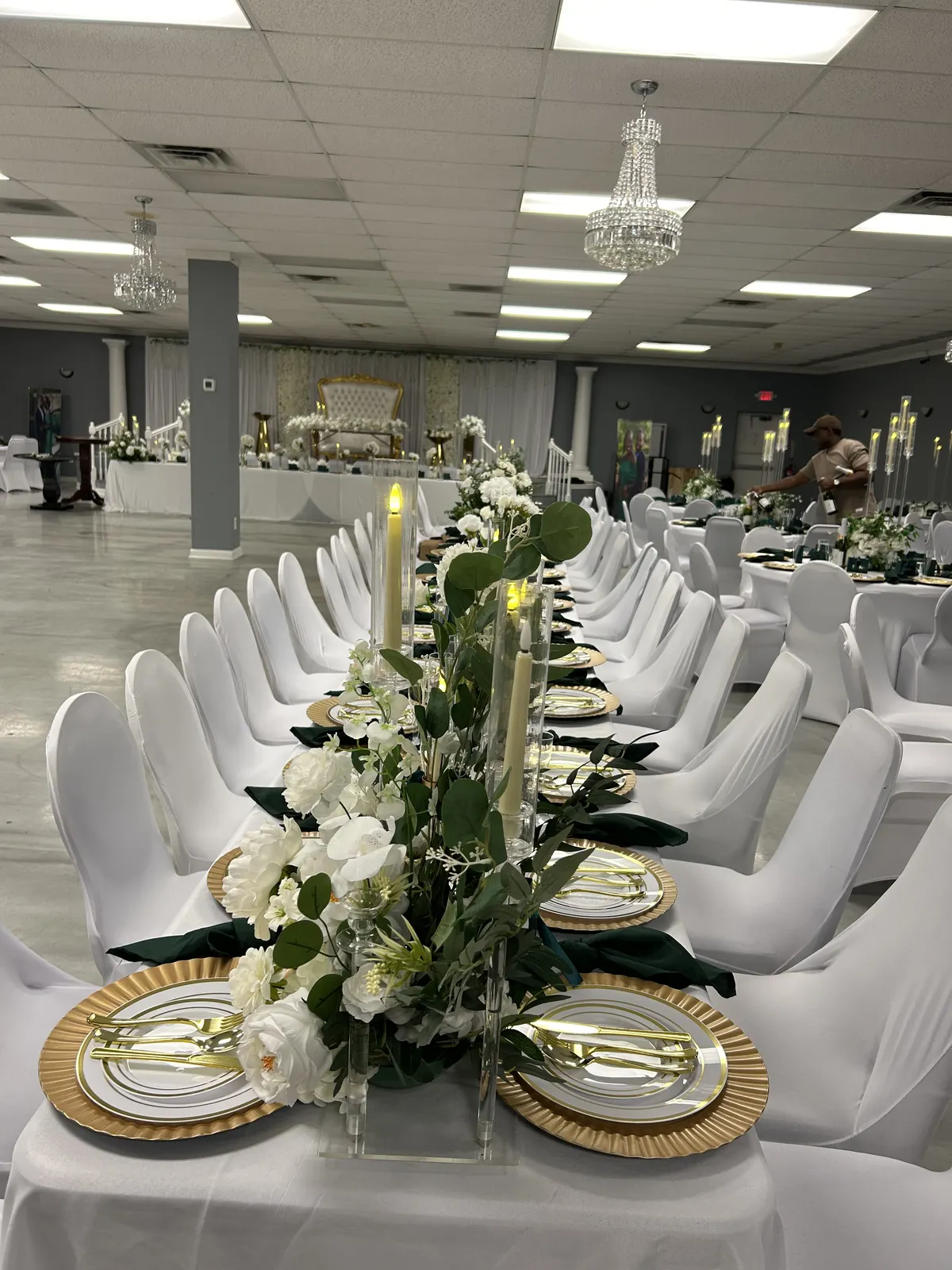 Wide white and emerald reception table with gold place settings and floral styling