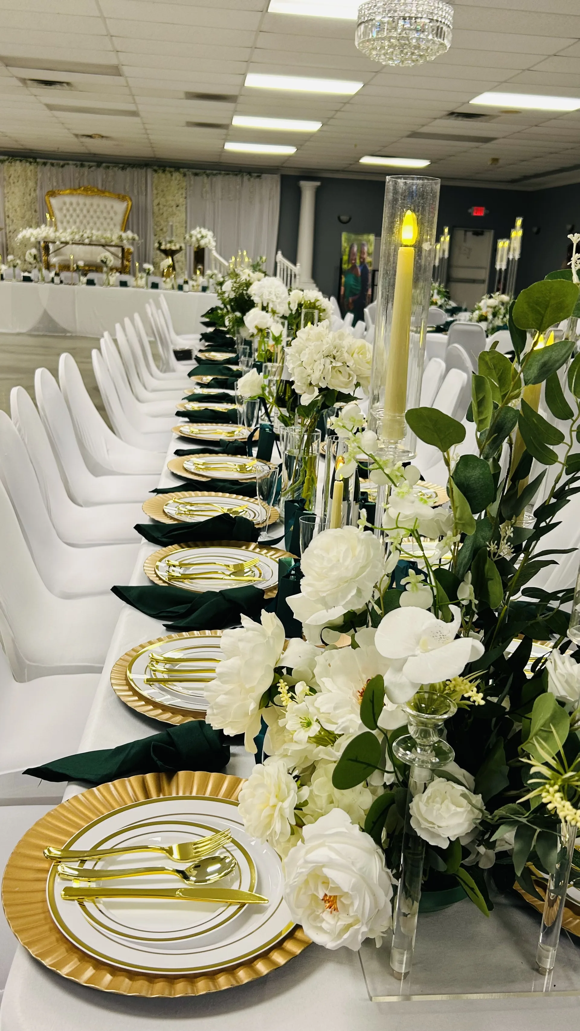 Long white and emerald reception table with white florals and gold place settings