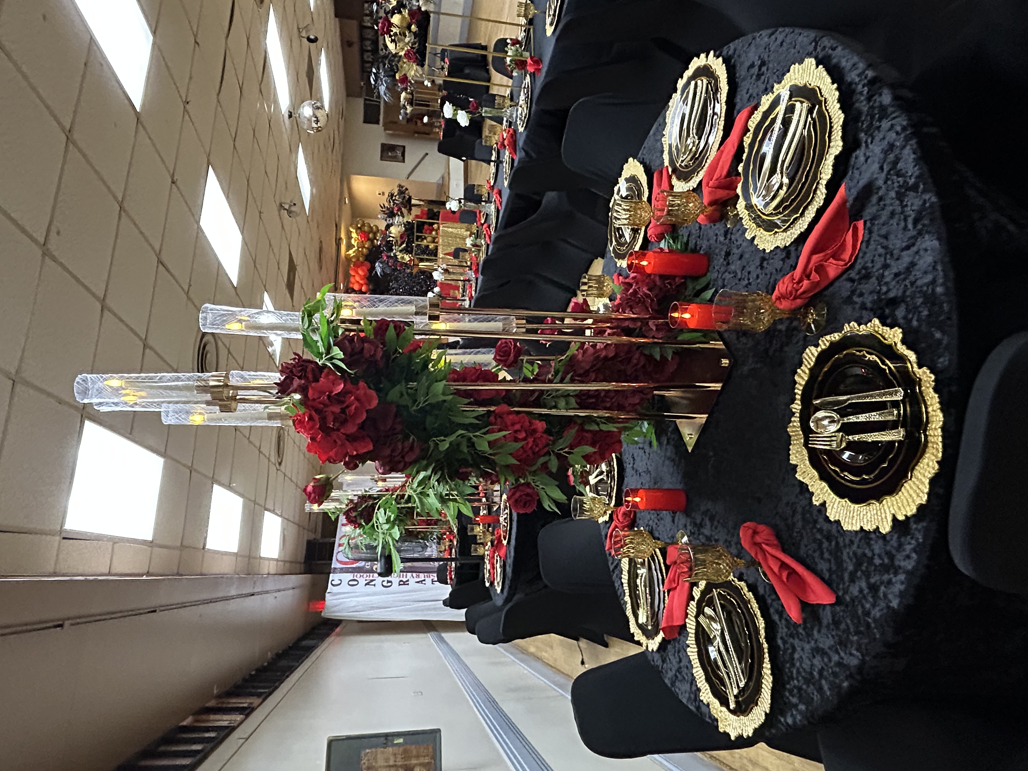 Full black velvet graduation table setup with red florals and gold chargers