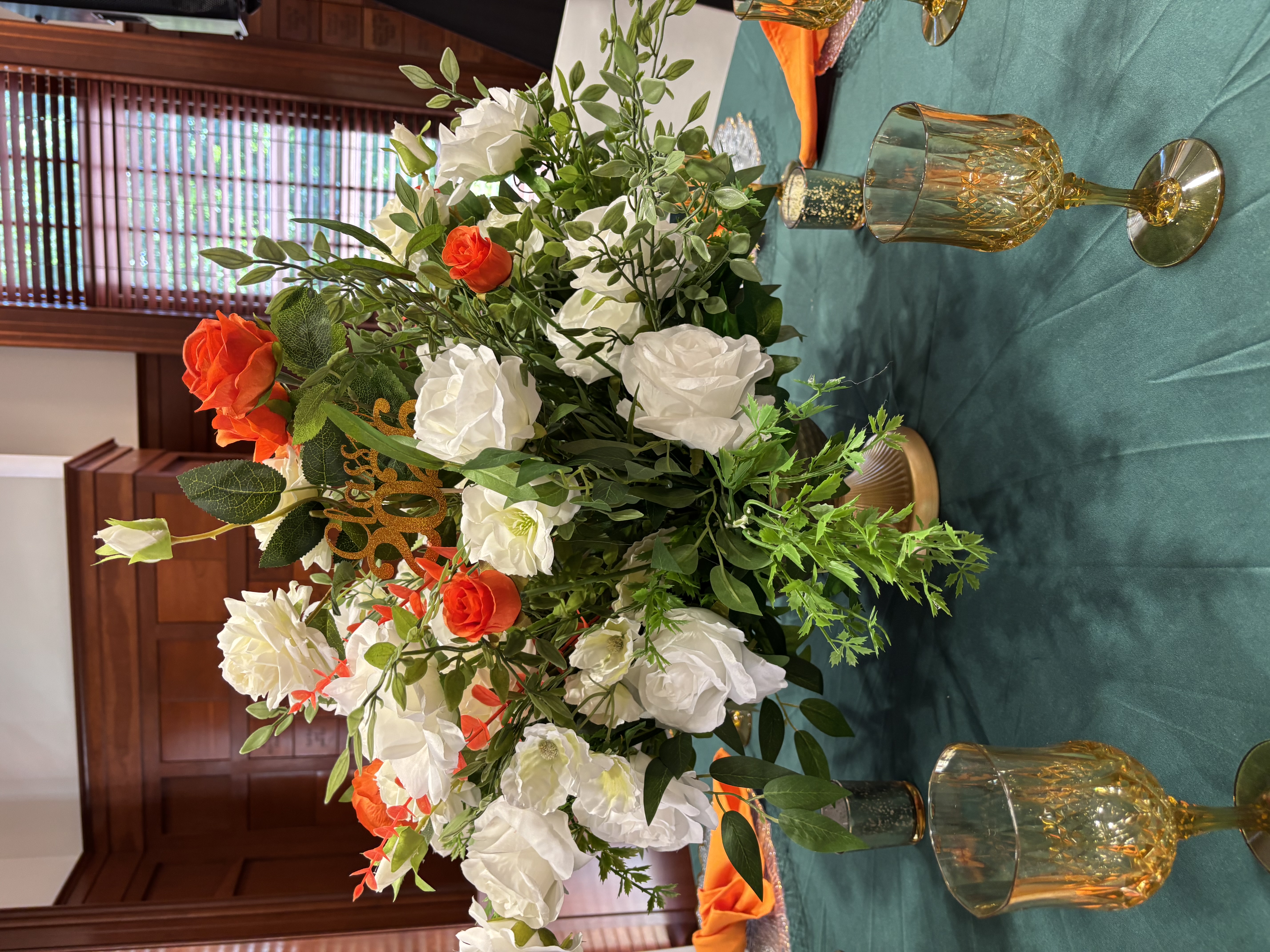 White and orange floral centerpiece on emerald tablecloth
