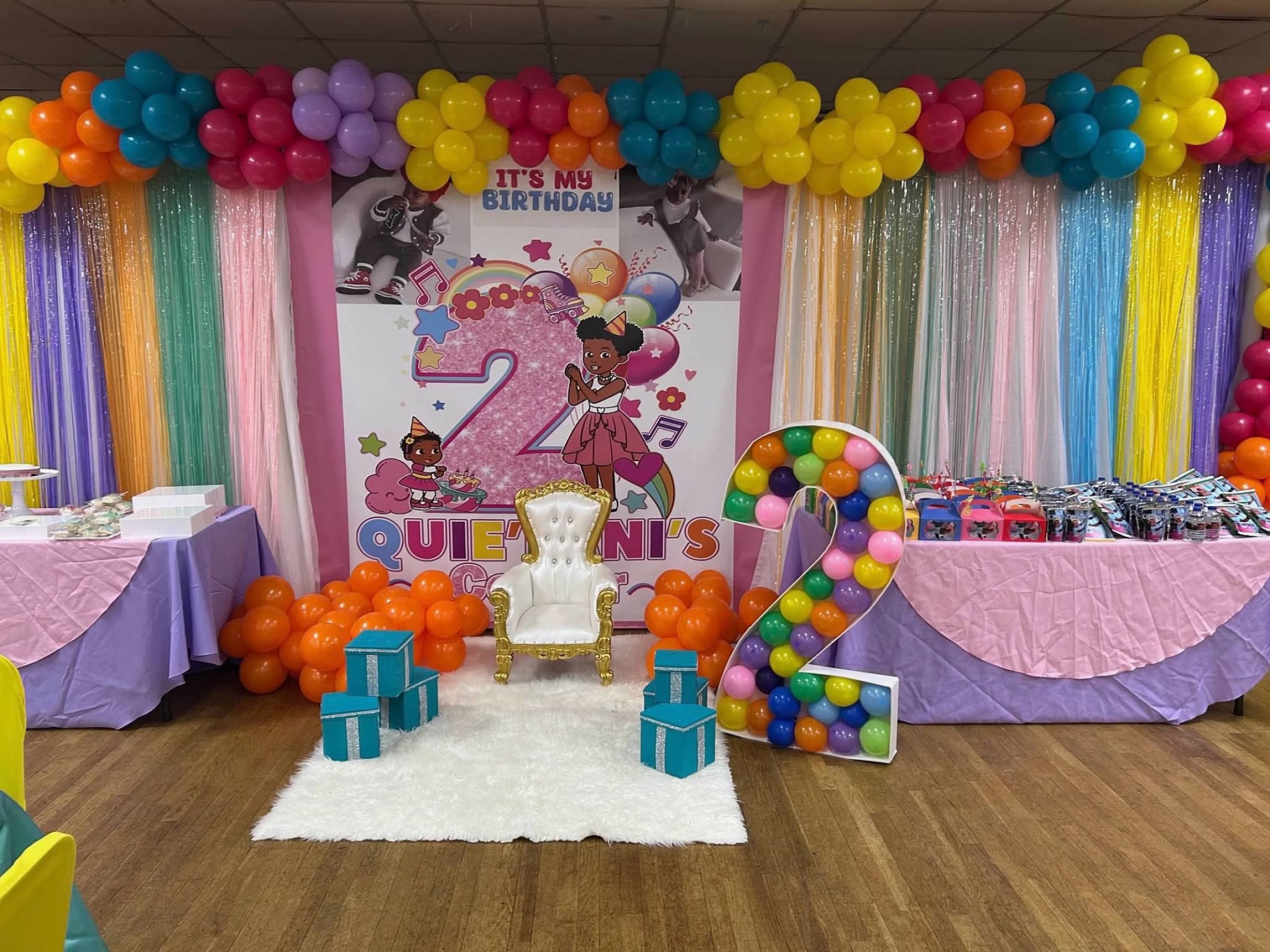 Colorful second birthday backdrop with balloon garland, throne chair, and balloon number
