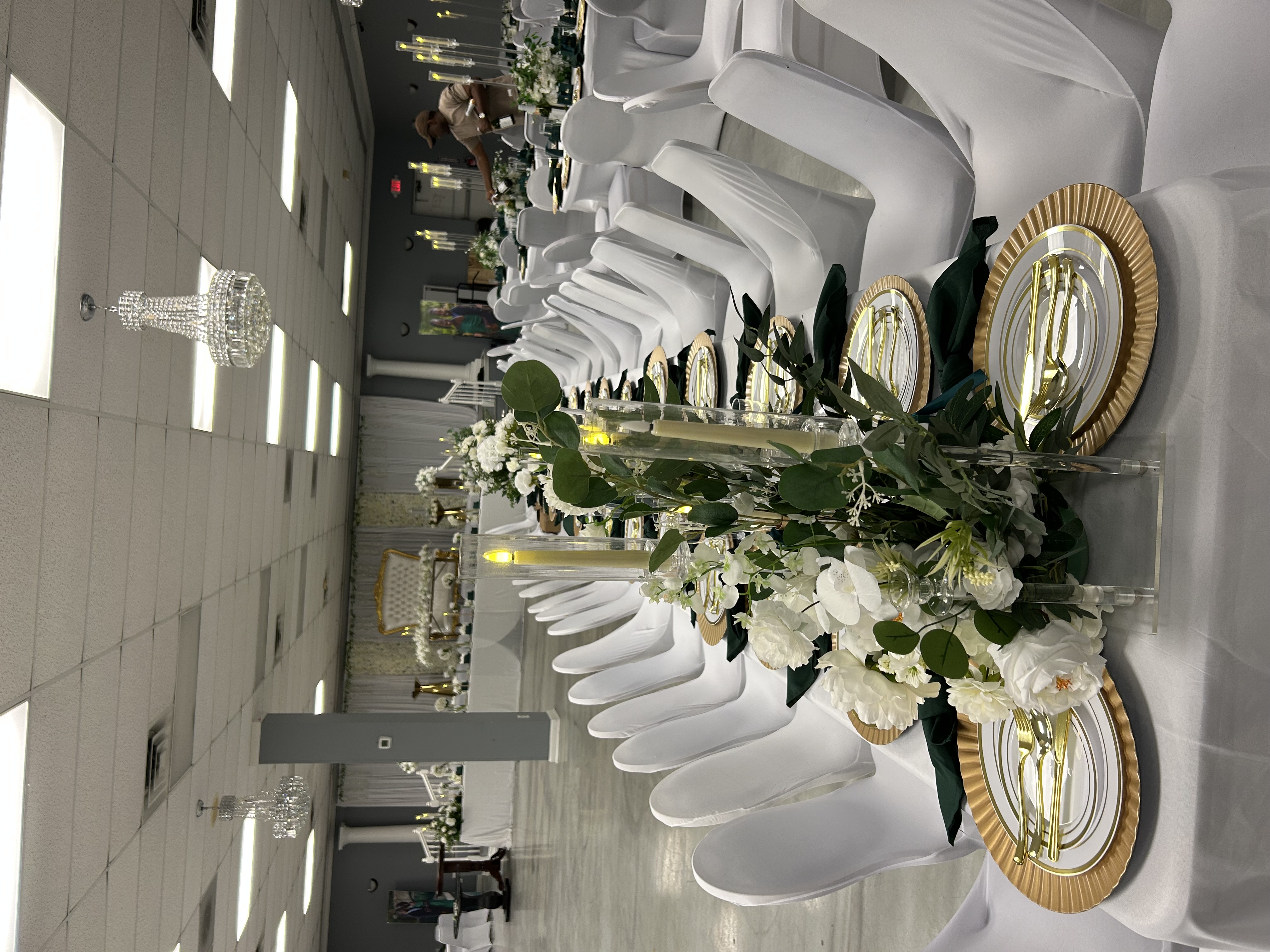 Wide white and emerald reception table with gold place settings and floral styling